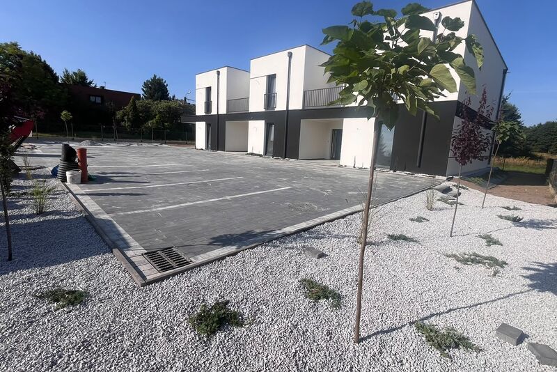 Parking z szarej kostki brukowej z wymalowanymi miejscami postojowymi przed budynkiem wielorodzinnym